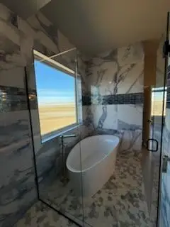 Modern bathroom featuring a freestanding tub, glass shower enclosure, and elegant marble walls with a scenic view outsides Modern bathroom featuring a freestanding tub, glass shower enclosure, and elegant marble walls with a scenic view outsides